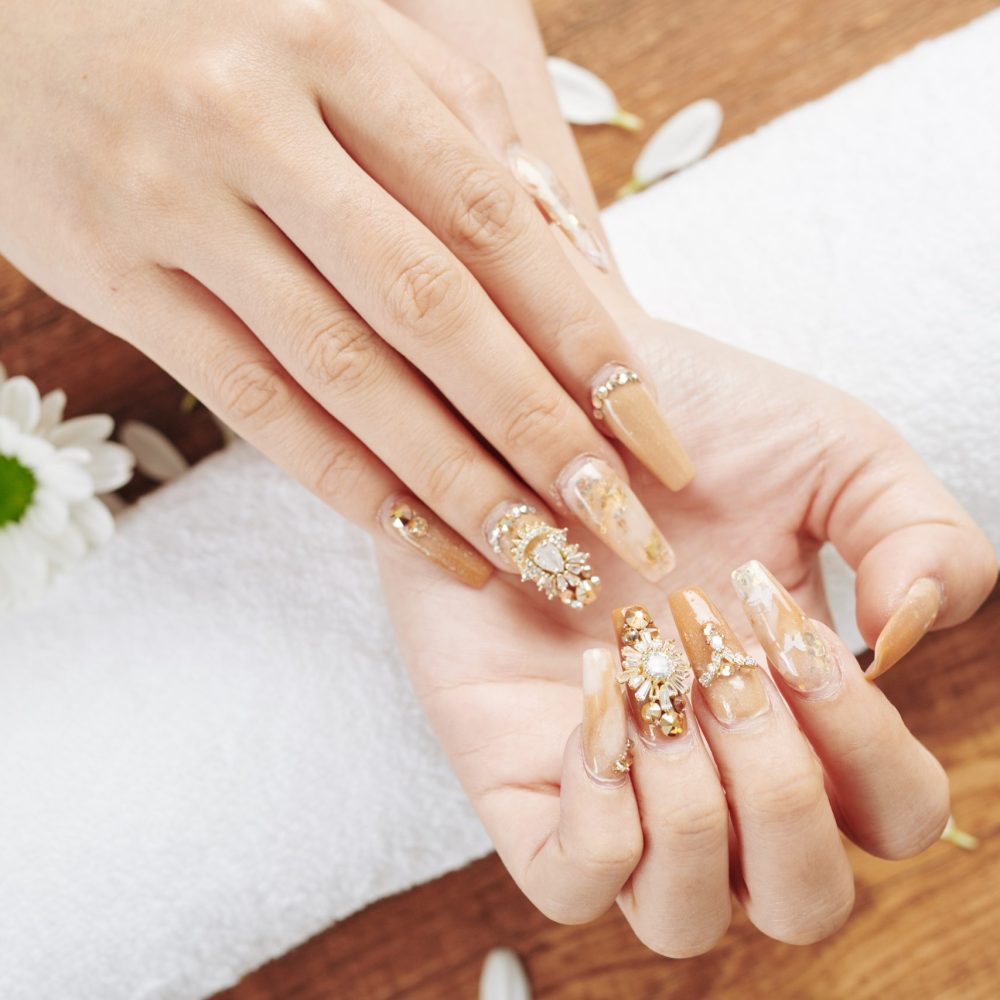 Woman showing her fancy creative manicure with golden polish and jewelry rhinestones